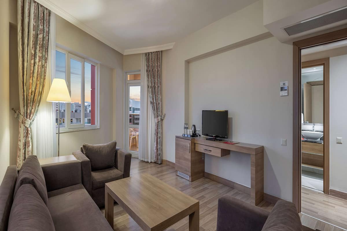A modern living room with a sofa, a coffee table, a TV on a wooden stand, and a view of the city through large windows.