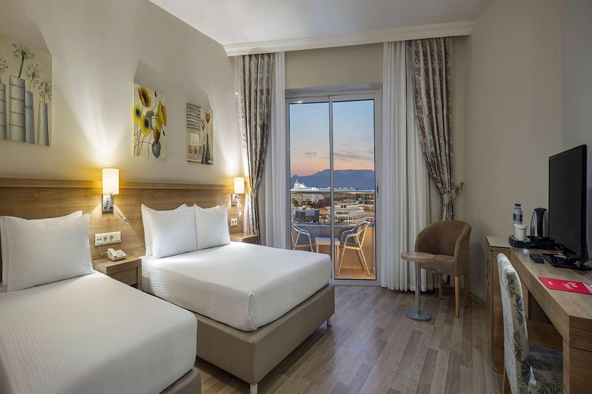 A hotel room with two beds, a desk, a chair, and a TV.