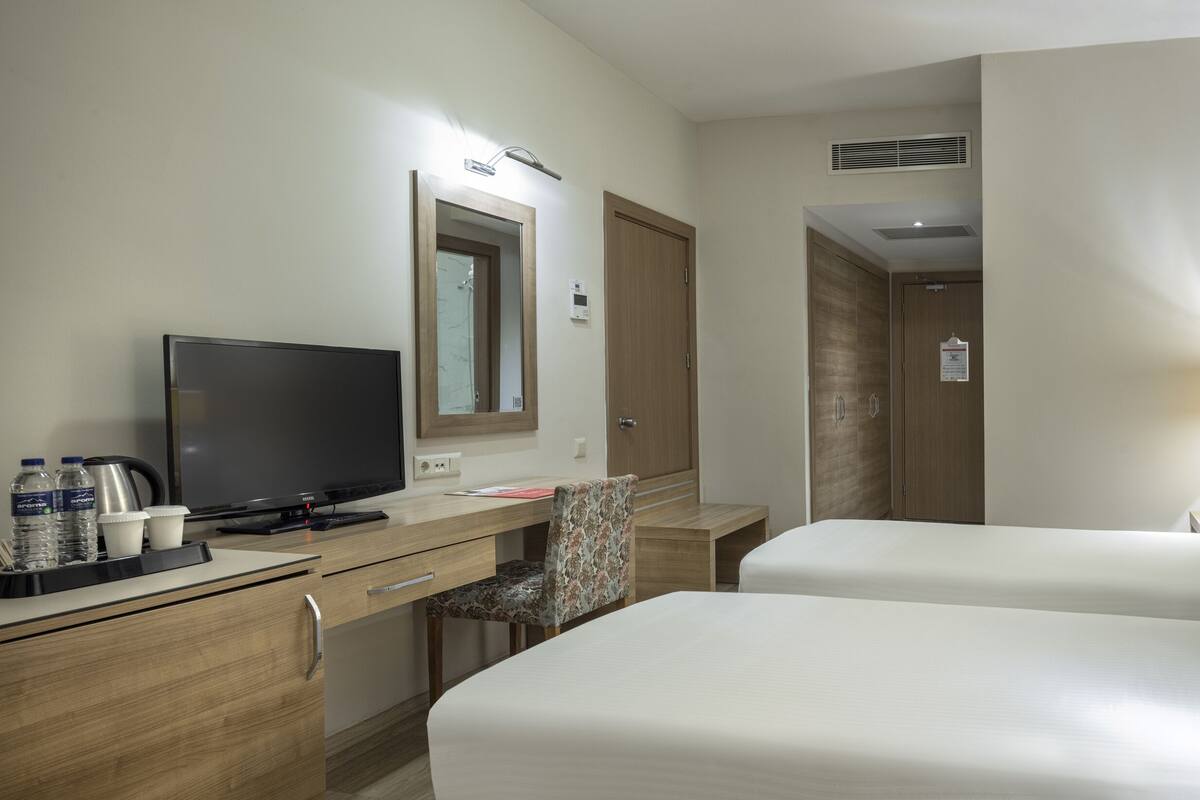 A hotel room with a desk, a television, a bed, a chair, and a lamp.