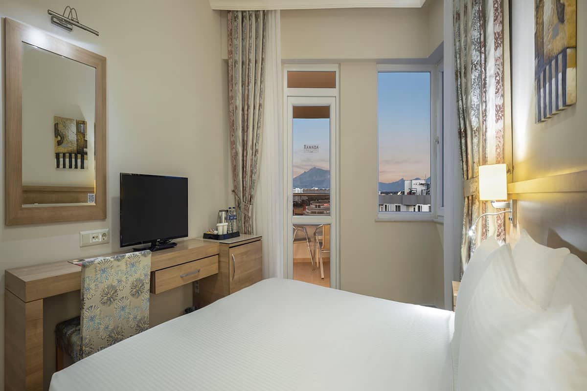 A hotel room with a bed, a desk, a television, and a view of a cityscape.