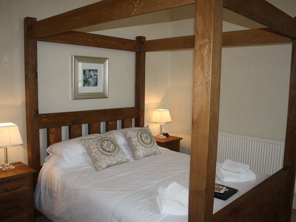 A bedroom with a wooden headboard, a framed picture on the wall, two bedside lamps, and neatly folded towels on the bed.