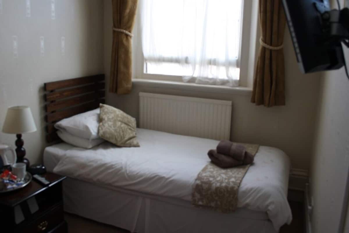 A single bed with a wooden headboard, a bedside table with a lamp, and a window with curtains.