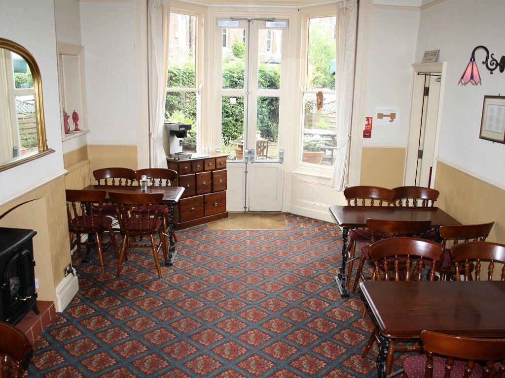 A dining area with a patterned carpet, wooden furniture, and a view through a door to an outdoor garden.