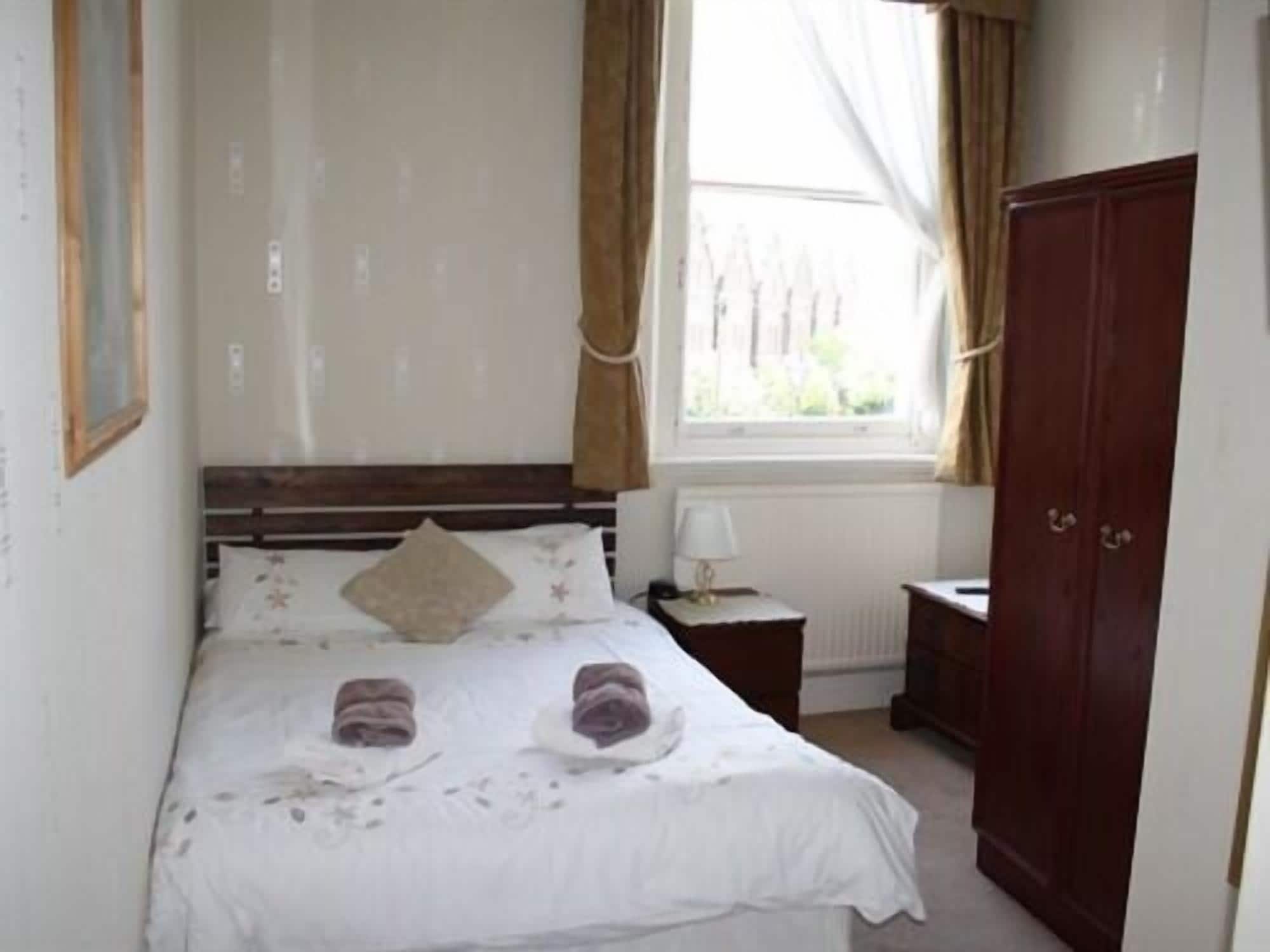 A bedroom with a bed, a nightstand, a wardrobe, and a window with curtains.