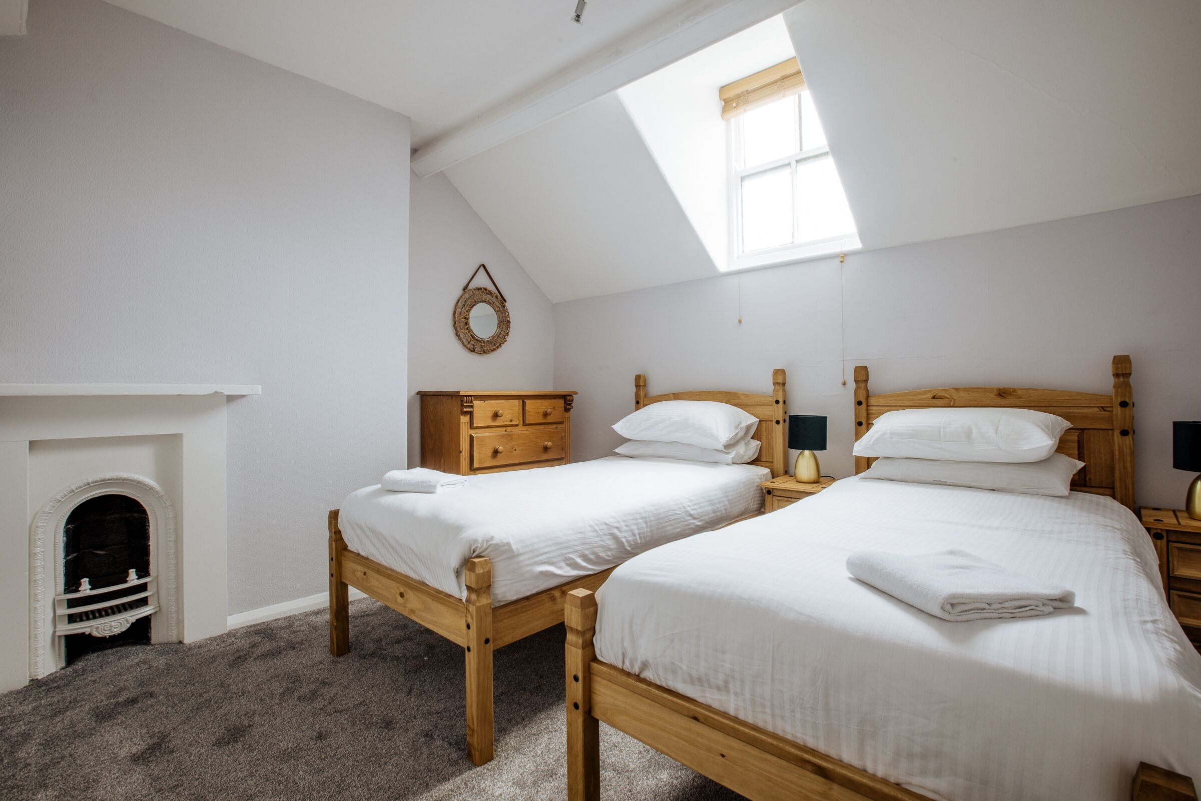 Een slaapkamer met twee houten bedden, een kleine open haard en een dakraam.