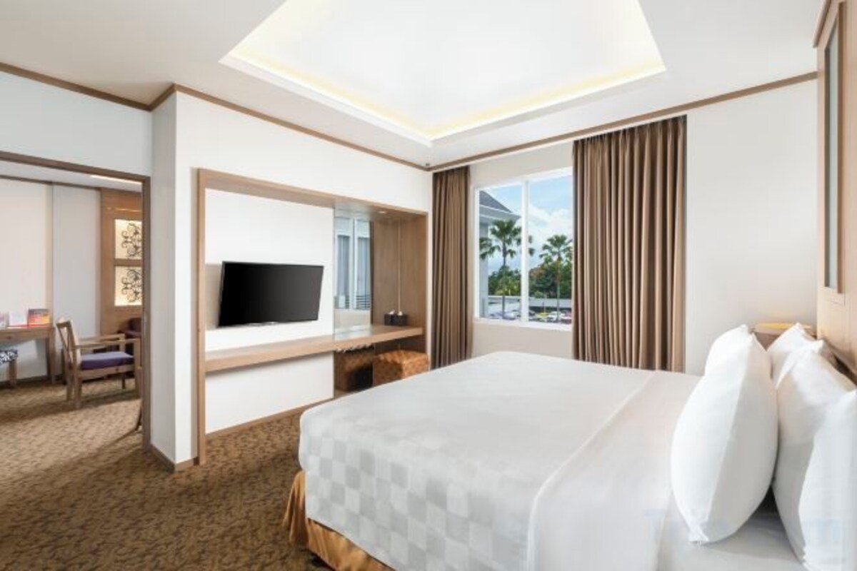 A hotel room with a large bed, a TV, a desk with a chair, and a window with curtains.