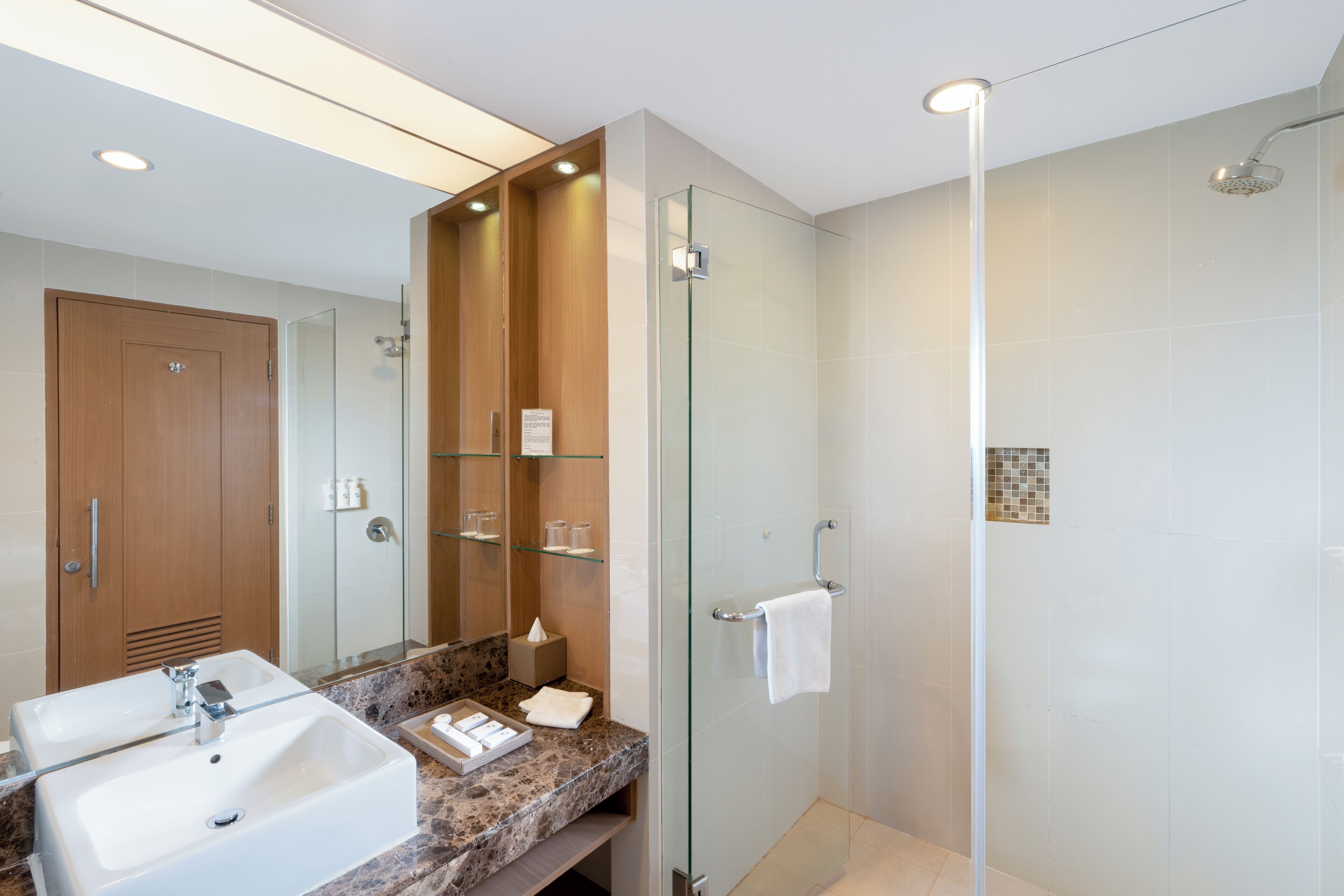 Een moderne badkamer met twee wasbakken, een douchecabine van glas en een houten wastafelmeubel.