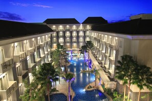 Un hotel con piscina central, varios balcones y palmeras.