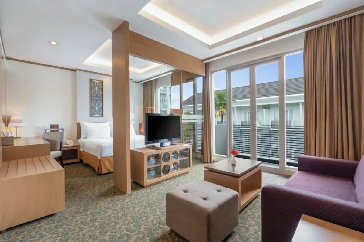 Habitación de hotel con cama, televisión, sofá, mesa de centro y una mesita de noche con lámpara.