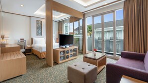 A modern hotel room with a large TV, comfortable seating, a small table, and a balcony with a view. - Swiss-Belhotel Danum Palangkaraya (Palangkaraya)