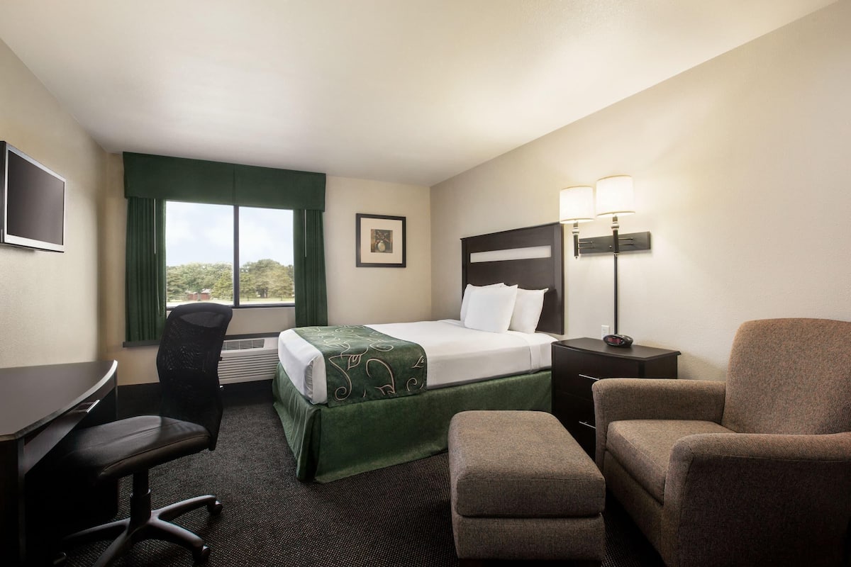 A hotel room with a bed, desk, chair, and a nightstand with lamps.