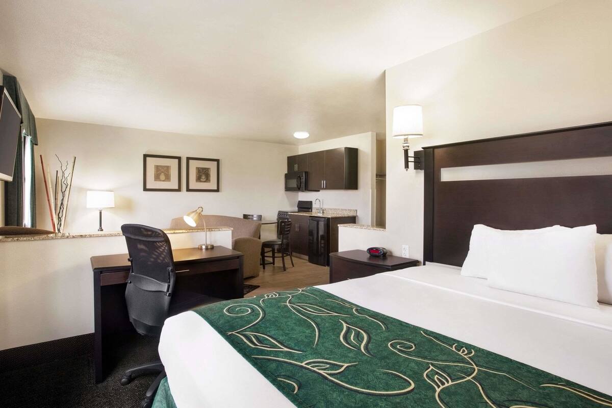 A hotel room with a bed, desk, chair, and kitchenette.