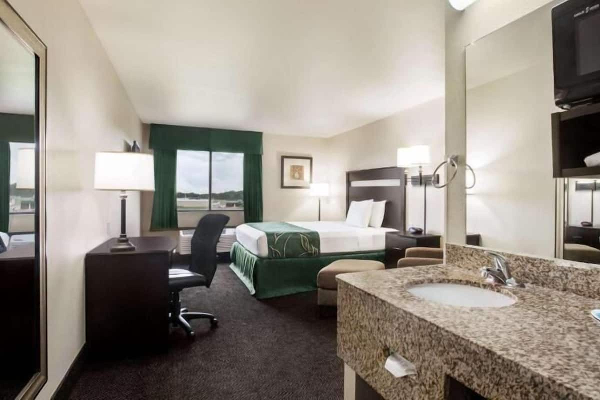 A hotel room with a bed, a desk, a chair, a sink, and a television.
