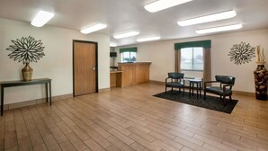 Um quarto espaçoso com piso de madeira, um balcão de recepção, uma área de refeições com cadeiras e duas peças de arte decorativa na parede.