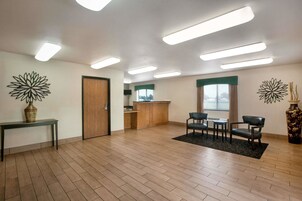 Um quarto espaçoso com piso de madeira, um balcão de recepção, uma área de refeições com cadeiras e duas peças de arte decorativa na parede.