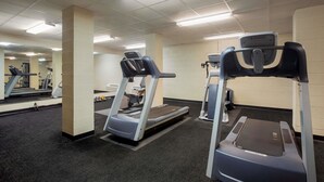 Uma academia com esteiras e equipamentos de exercícios, piso coberto por carpete e um espelho na parede.