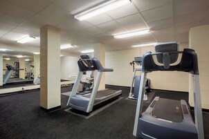 Uma academia com esteiras e equipamentos de exercícios, piso coberto por carpete e um espelho na parede.