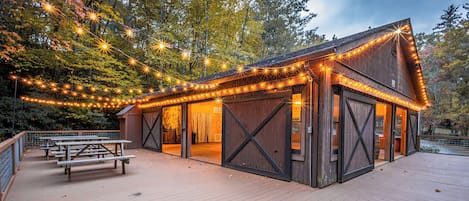 A wooden cabin with string lights, a covered patio, and picnic tables.