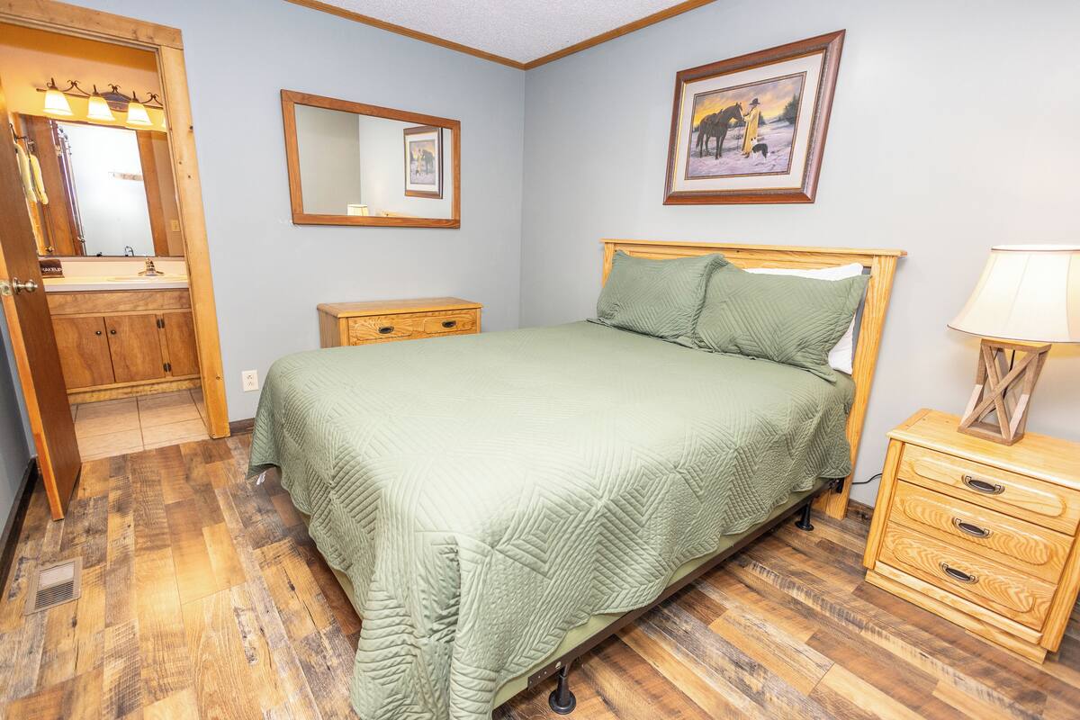 Une chambre à coucher avec un lit en bois, une table de chevet, une commode, un miroir et un tableau encadré accroché au mur.