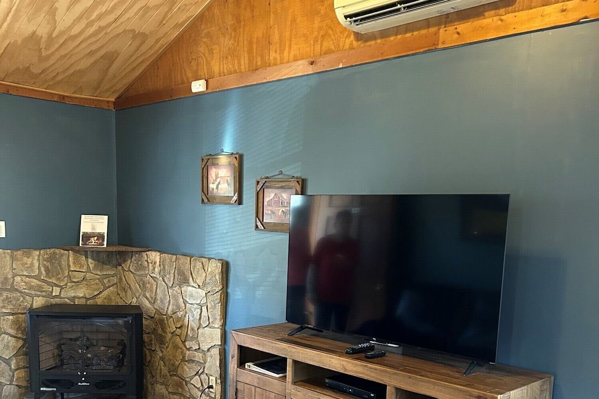 Un salon doté d’une cheminée en pierre, d’un meuble de rangement en bois pour les appareils électroniques et d’un climatiseur fixé au mur.
