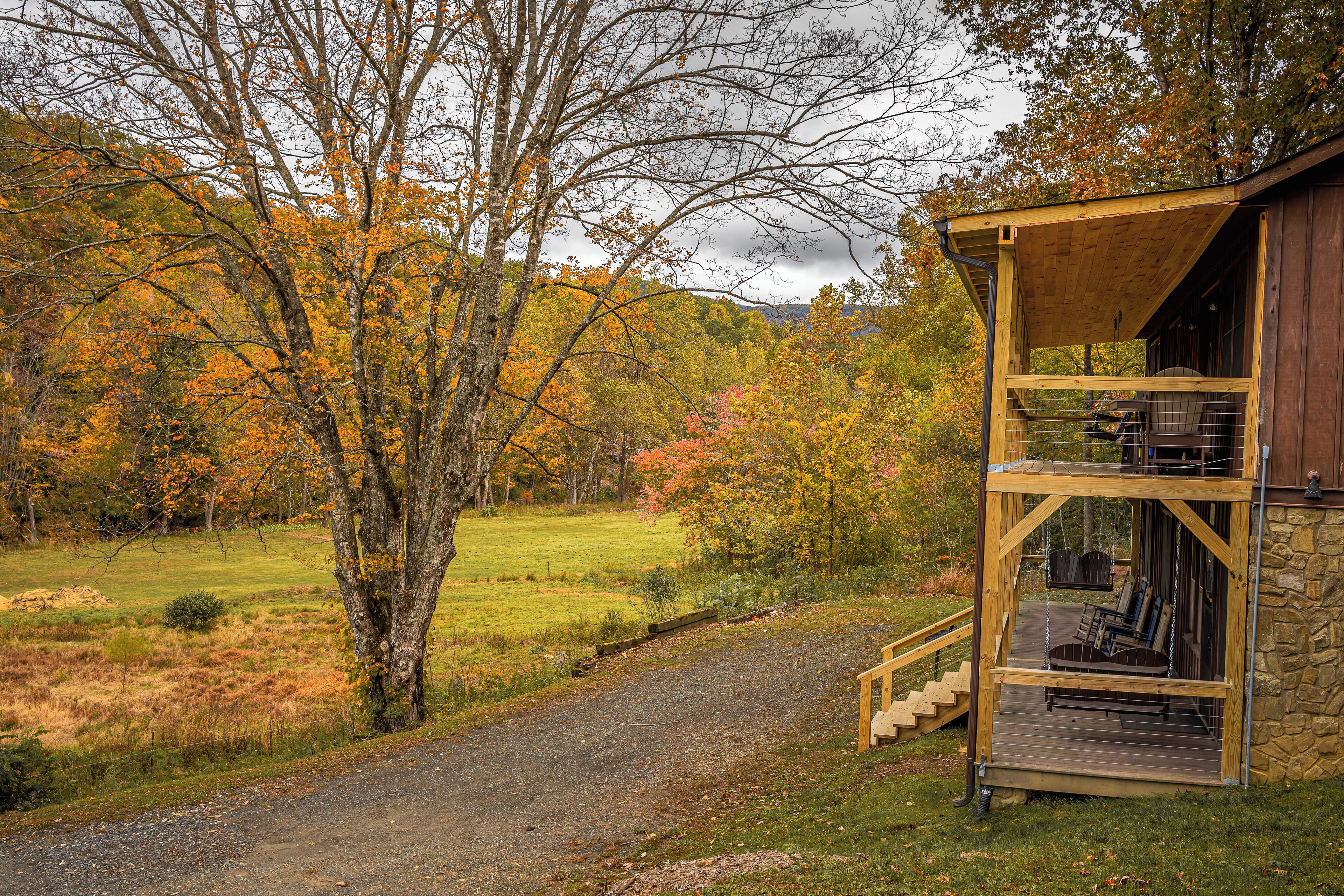 A rustic cabin with a wooden deck and stone walls, surrounded by autumn foliage.