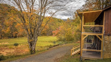 A rustic cabin with a wooden deck and stone walls, surrounded by autumn foliage.