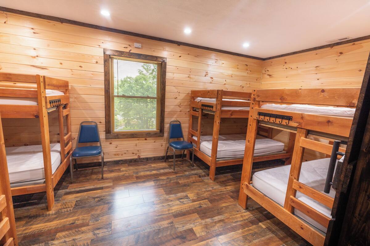 Une pièce avec quatre lits superposés en bois, une fenêtre avec des stores et une chaise bleue.