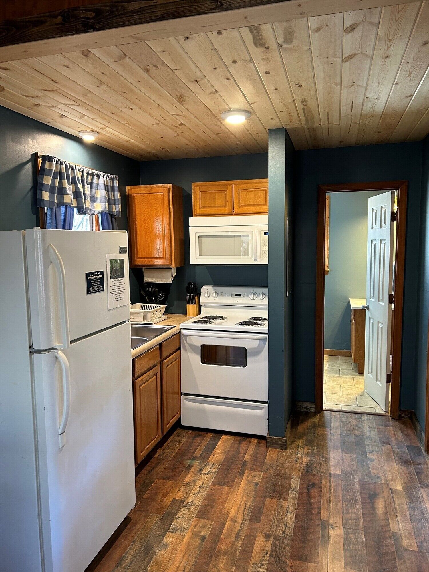 A compact kitchen with wooden cabinets, a white refrigerator, a microwave, and a stove.