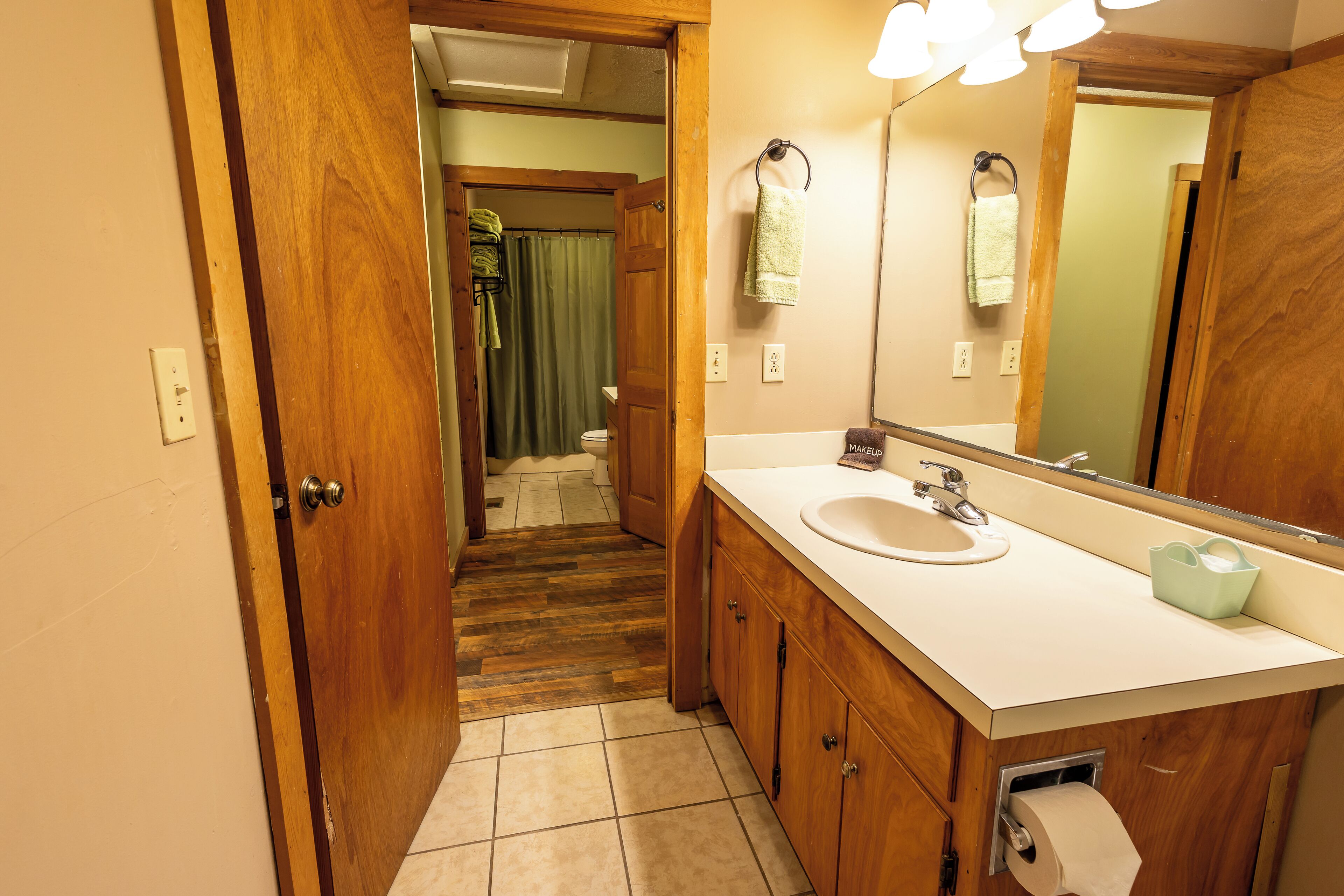A bathroom with a wooden door, a sink, a mirror, and a toilet visible in the background.