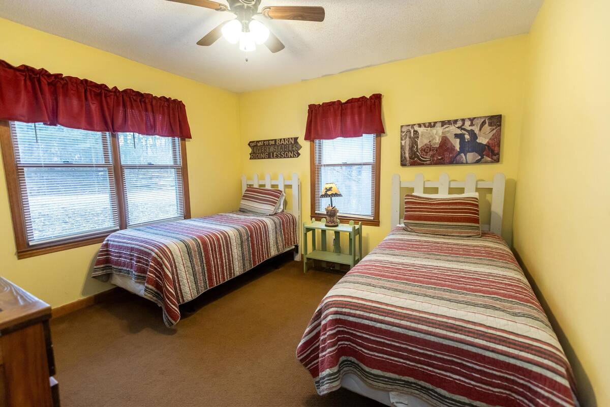 Une chambre avec deux lits, un ventilateur de plafond et une fenêtre avec des stores.