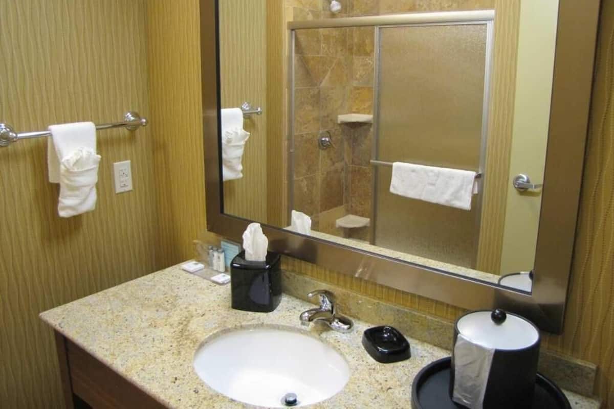 A bathroom with a sink, mirror, towel rack, and a shower area.