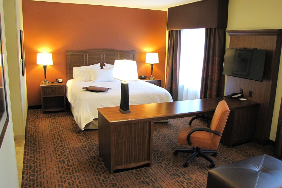 A hotel room with a bed, bedside tables with lamps, a desk with a chair, and a television on the wall.