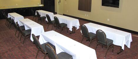 A conference room with multiple tables and chairs, a television mounted on the wall, and a door with a sign.