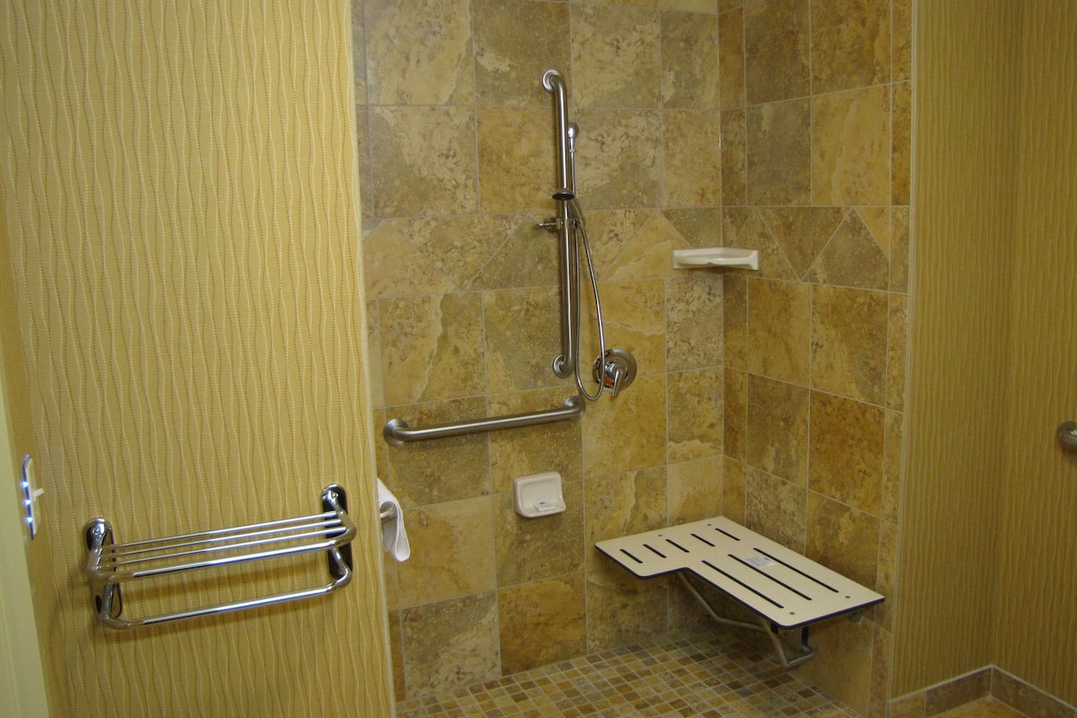 A bathroom with a shower, grab bars, a hand dryer, and a tiled floor.