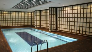 Une piscine dotée d’un plancher en bois et de murs carrelés, entourée d’une cloison en bois avec un motif en forme de grillage.