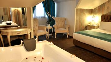 A hotel room with a large bathtub, a bed, a desk with a mirror, two armchairs, and a nightstand with a lamp.