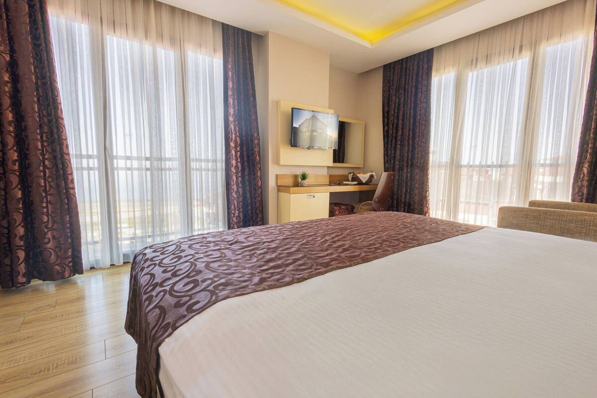 Habitación de hotel con una cama grande, un escritorio, una silla, un televisor y cortinas.
