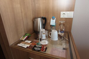 Un mini bar de hotel con una cafetera, una botella de agua, un vaso de agua y varias bolsitas de café y té.