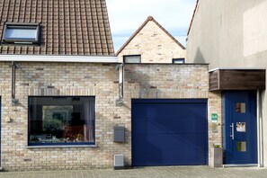 A building with a brick facade, a large garage door, and a blue door with a sign above it. - B&B Lievejan (Jabbeke)