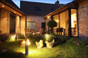 Een bakstenen huis met een patio, met twee vogelbeeldjes, een tafel en stoelen.
