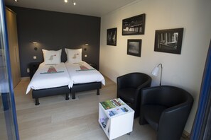 A bedroom with a double bed, two bedside tables, a nightstand, a small white side table with magazines, two black chairs, and framed pictures on the wall. - B&B Lievejan (Jabbeke)