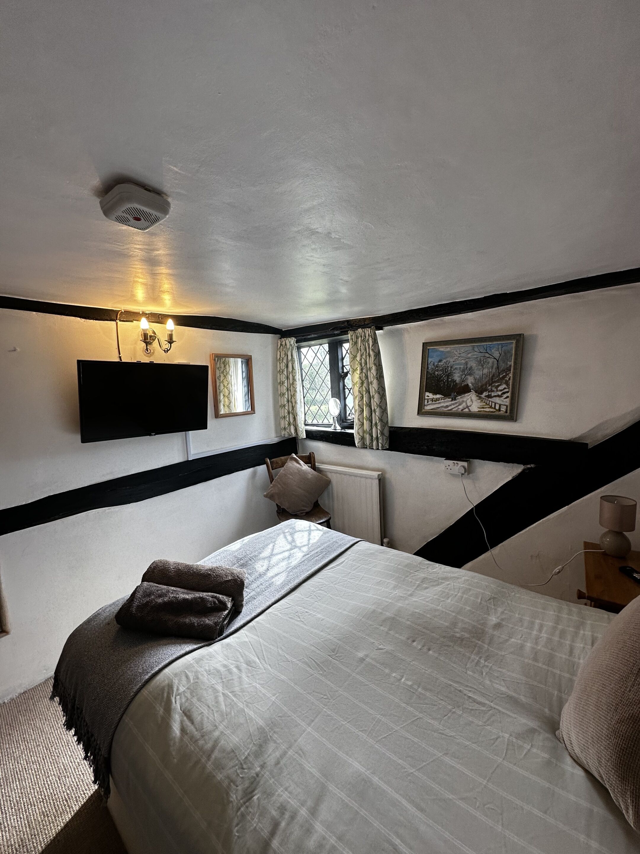 A bedroom with a bed, a TV mounted on the wall, a window with curtains, and a painting on the wall.