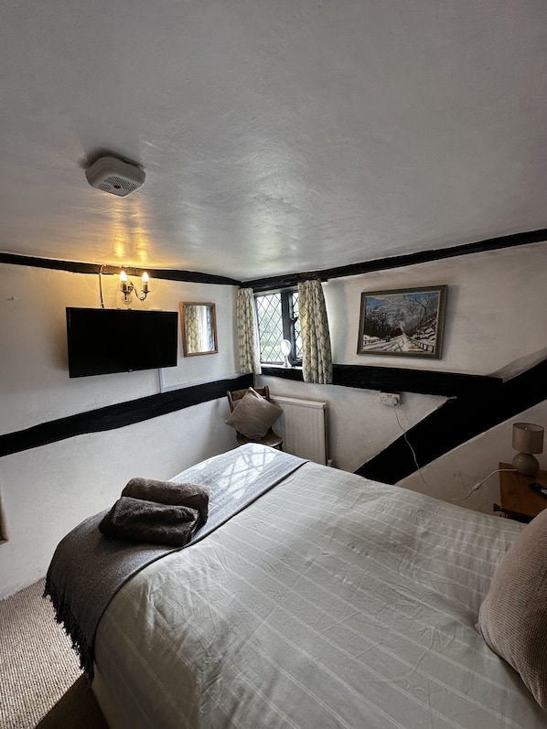 Un dormitorio con cama, televisor montado en la pared, ventana con cortinas y un cuadro colgado.