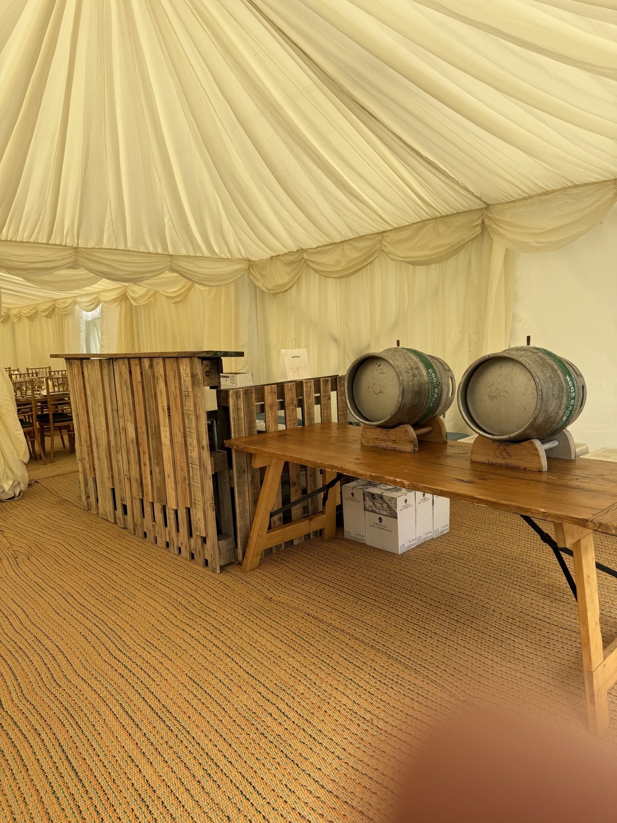 A tented area with a wooden table, two barrels, and a bar counter.