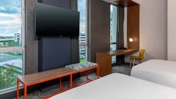 A hotel room with a bed, a desk, a chair, a bench, and a TV mounted on the wall.