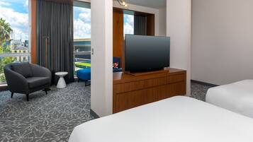 Una camera d'albergo con un letto, una TV su un mobile in legno, una sedia, un tavolino e vista sull'esterno.