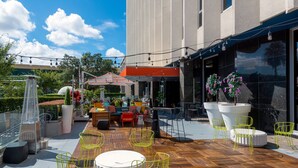 An outdoor patio with wooden flooring, yellow chairs, a round table, and a seating area with sofas and a red umbrella.