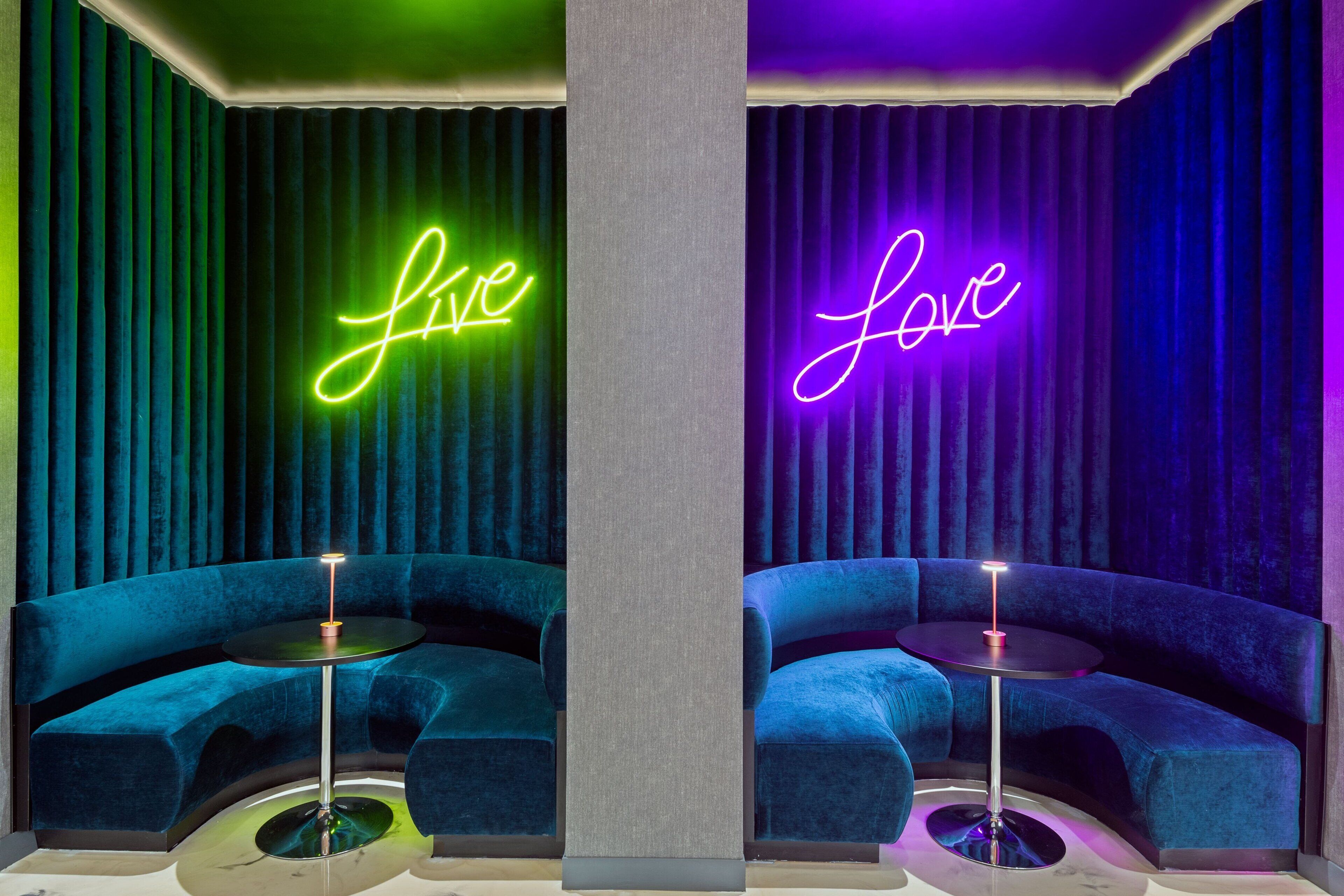 Ett rum med två blå sammetssoffor, en central pelare och neonljusskyltar med orden ”live” och ”love”.