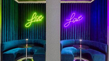 Ett rum med två blå sammetssoffor, en central pelare och neonljusskyltar med orden ”live” och ”love”.