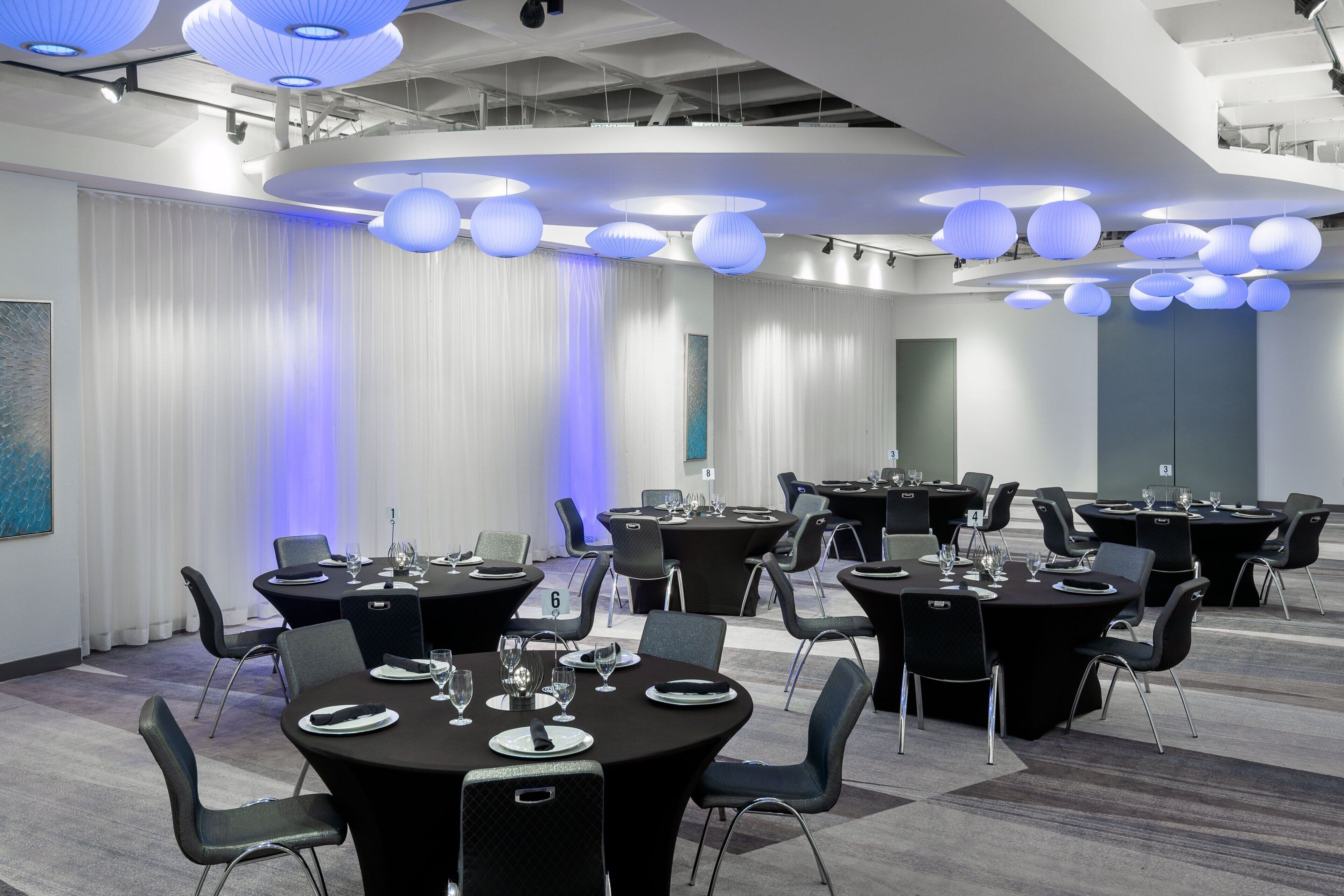 Una sala de conferencias moderna con mesas redondas, sillas negras e iluminación azul.